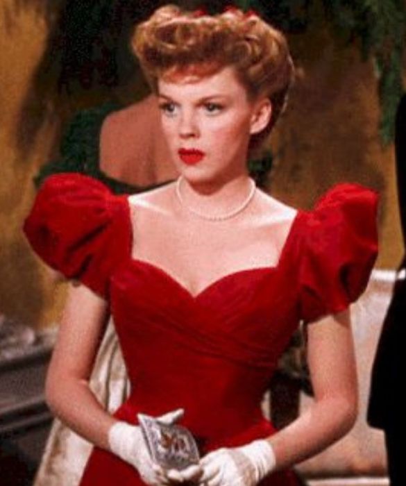 <p>Dopo le scarpette rosse (ne <em>Il mago di Oz</em>, naturalmente) il <strong>vestito rosso</strong>. Infatti, vi viene in mente qualcosa di pi&ugrave; natalizio di un abito rosso? Quello di <strong>Judy Garland</strong> in uno dei pi&ugrave; grandi classici film di Natale &egrave; di una magnifica tonalit&agrave; di rosso acceso, ha lo <strong>scollo a cuore</strong> incrociato e le <strong>maniche a sbuffo</strong>. A dare quel tocco in pi&ugrave;, un filo di perle, il rossetto rosso in tinta con l&rsquo;abito e un paio di guanti bianchi: il massimo dell&rsquo;eleganza, per chi si sente&nbsp;perdutamente innamorata della magia del Natale.</p>
