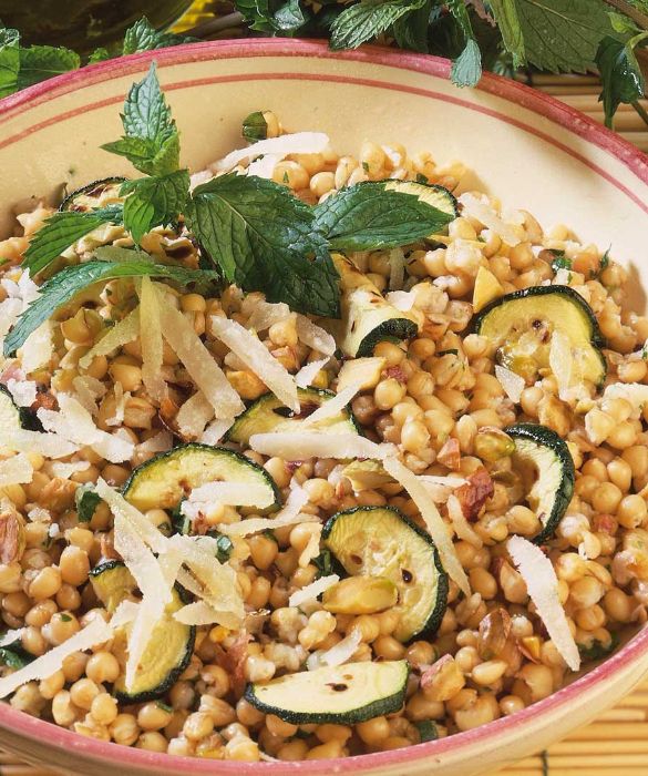 Per realizzare 4 piatti di Grano con zucchine, pistacchi e pecorino fate cuocere 300 g di grano precotto in una pentola con abbondante acqua bollente salata, seguendo attentamente le indicazioni dei tempi riportati sulla confezione. Sbollentate un cucchiaio di pistacchi sgusciati, sgocciolateli, fateli intiepidire, privateli della pellicina che li ricopre e poi tritateli grossolanamente. Lavate accuratamente 4 zucchine, asciugatele con un telo da cucina e, dopo averle spuntate, tagliatele a fettine oblique. Procedete quindi a grigliarle sulla piastra rovente per 30 secondi circa per ciascuna parte. Raccogliete quindi le zucchine in una terrina e conditele con un pizzico di sale, una generosa macinata di pepe, 1 cucchiaio d’olio e un ciuffo di menta sminuzzata. Tritate grossolanamente 50 g di pecorino fresco e riducete a scaglie sottili 30 g di pecorino stagionato. Sgocciolate bene il grano e lasciatelo intiepidire, quindi mescolatelo alle zucchine e condite il tutto con 3 cucchiai d’olio d’oliva e poche gocce di succo di limone. Unite al grano i pistacchi e i formaggi e mescolate bene il tutto. Trasferite la preparazione su un piatto da portata, decorate con qualche fogliolina di menta, lavata e asciugata delicatamente, e portate subito in tavola.