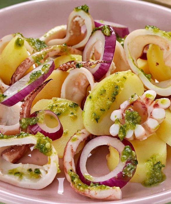 Per 4 porzioni di insalata di totani e patate con pesto di pistacchi, lessate 400 g di patate a pasta gialla in acqua salata per 30-40 minuti dal momento del bollore. Pulite 600 g di totani: separate le sacche dalle teste, poi da queste ultime eliminate con un paio di forbici le interiora, la cartilagine, gli occhi e il becco all’attaccatura dei tentacoli. Private le sacche della pelle, tirandola a partire dall’apertura verso la punta. Riunite le sacche e le teste in una casseruola, coprite a filo con del brodo vegetale, unite mezzo bicchiere di vino bianco secco, 1 foglia di alloro e un ciuffo di prezzemolo, portate a bollore e lasciate cuocere per 5-10 minuti (il tempo dipende dalla loro grandezza). Scolate i totani, fateli raffreddare e tagliate le sacche ad anelli. Sbucciate due cipolle rosse e tagliatele a rondelle. Scolate le patate, fatele raffreddare, pelatele e tagliatele a fettine. Frullate uno spicchio d'aglio sbucciato e privato dell’eventuale germoglio con 2 cucchiai di pistacchi sgusciati, unite mezzo mazzetto di foglie di rucola e un mazzo di foglie di basilico lavate e asciugate, una presa di sale e un pizzico di pepe e continuate a frullare, unendo a filo l’olio necessario a ottenere un pesto non troppo denso. Riunite in un piatto le patate, le cipolle e i totani, condite con qualche cucchiaio del pesto preparato e servite.