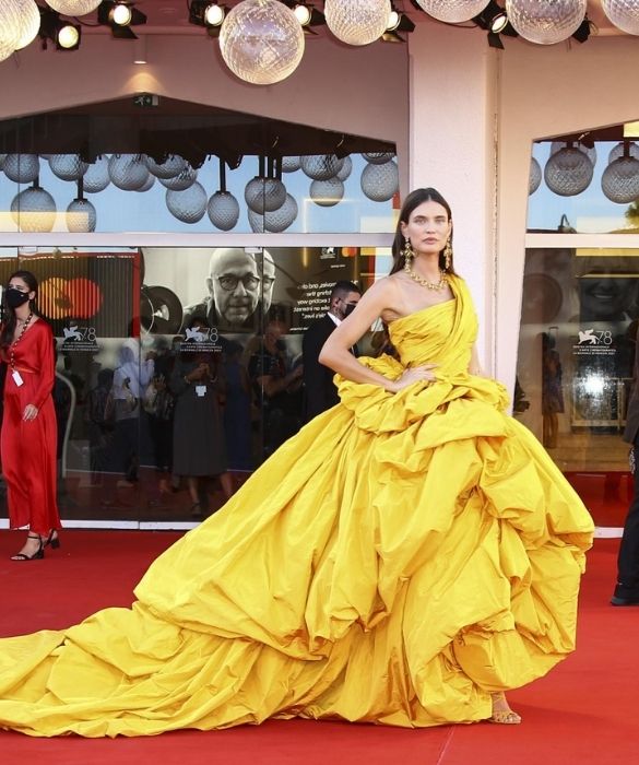<p>La musa di <strong>Dolce&Gabbana</strong> sembra un sole dorato, nel suo monumentale abito giallo monospalla. Volumi esagerati e lungo strascico per un sontuoso capo <strong>haute couture</strong>, composto da drappeggi asimmetrici e balze stropicciate. Il massimalismo al suo massimo splendore, anche grazie agli importanti <strong>gioielli</strong>: grandi orecchini a croce e collier, accomunati da maxi gemme quadrate. Per brillare come nessun&rsquo;altra.</p>
