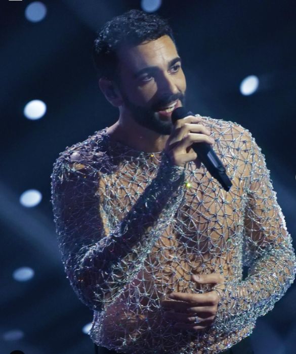 <p>E la sua <strong>maglia metallica</strong>, proprio come dice la canzone <em>Due Vite</em>, il successo con cui ha vinto a Sanremo 2023. Marco Mengoni torna in <strong>Versace</strong> (squadra che vince non si cambia) in una veste nuova, quella di co-conduttore, dalle inaspettate doti di intrattenitore d'insospettabile freschezza. Sul palco si presenta con due completi in pelle, tra cui un tailleur con gonna deliziosamente <strong>gender fluid</strong>, ma il nostro look preferito &egrave; quello che lo fa brillare di pi&ugrave;. E il due pezzi composto da <strong>maglia-gioiello traforata con cristalli</strong> e pantalone sartoriale lo fa decisamente risplendere nel firmamento sanremese.</p>

